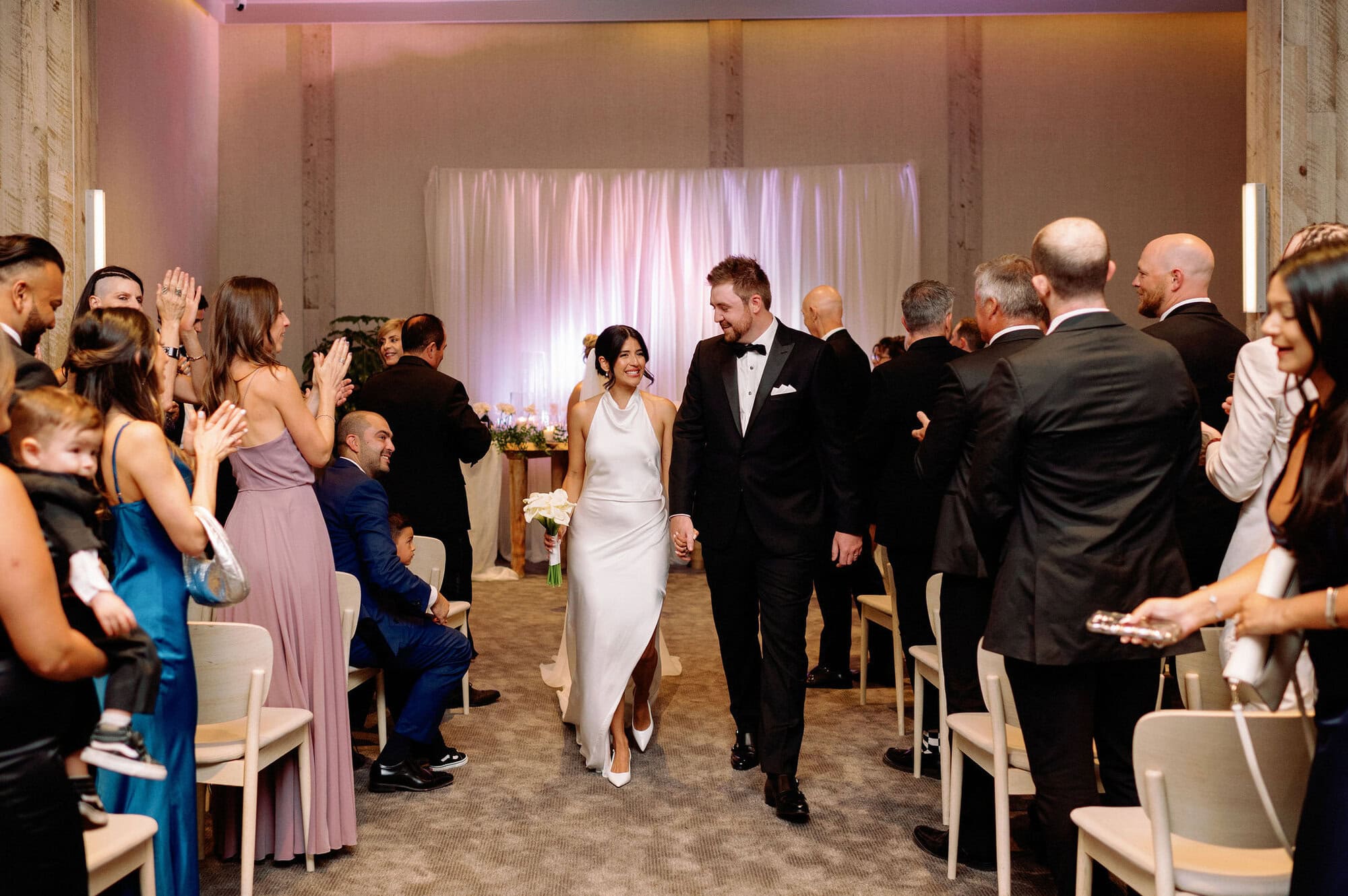 Bride and groom walk down ceremony aisle at 1 Hotel Toronto as guests cheer