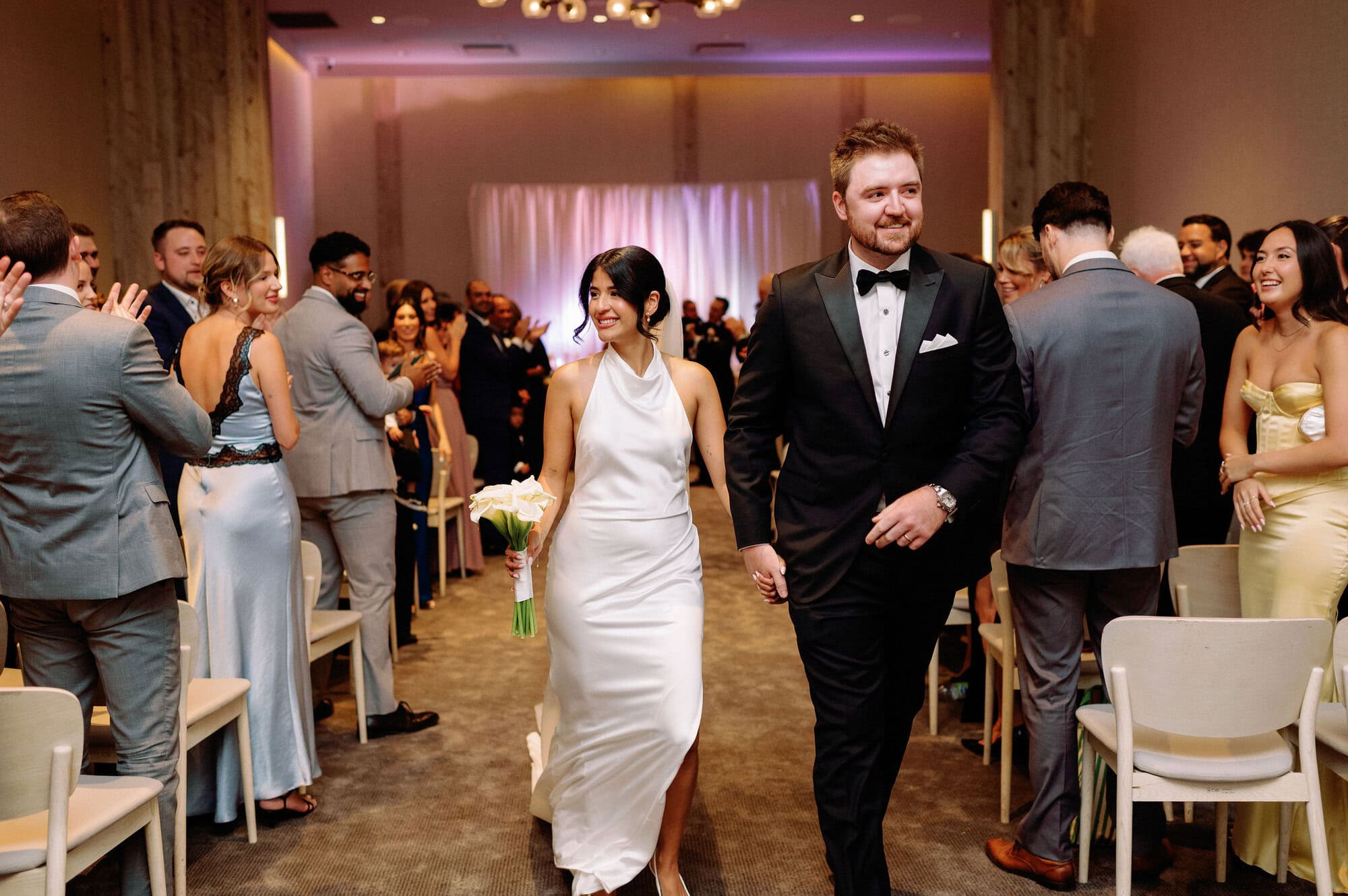 Bride and groom walk down ceremony aisle at 1 Hotel Toronto as guests cheer