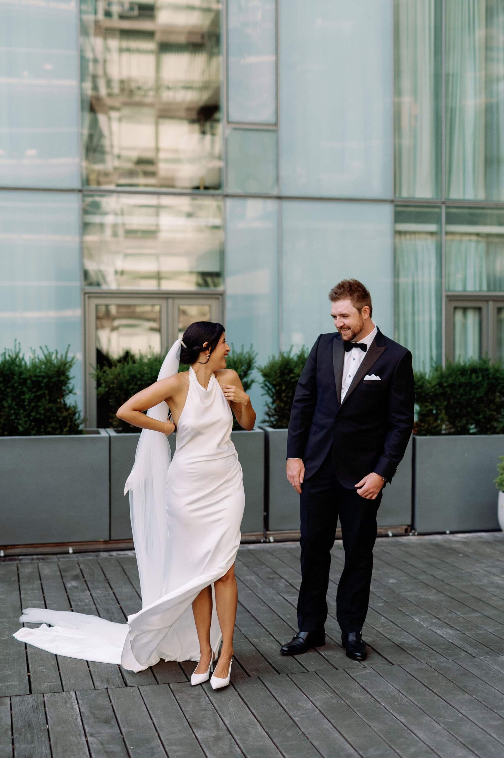 Bride adjusting her gown during portraits outside 1 Hotel Toronto while the groom watches.