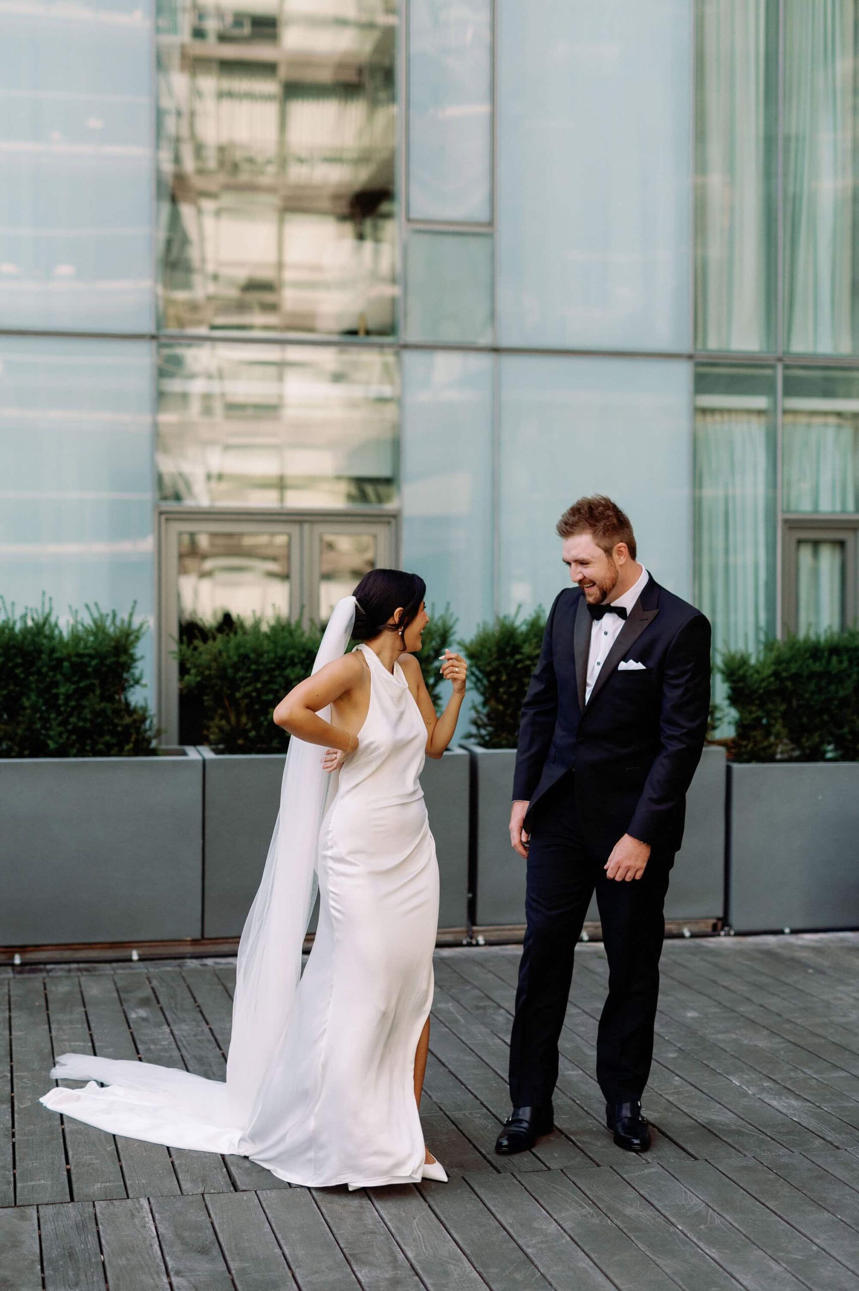 Bride adjusting her gown during portraits outside 1 Hotel Toronto while the groom watches.