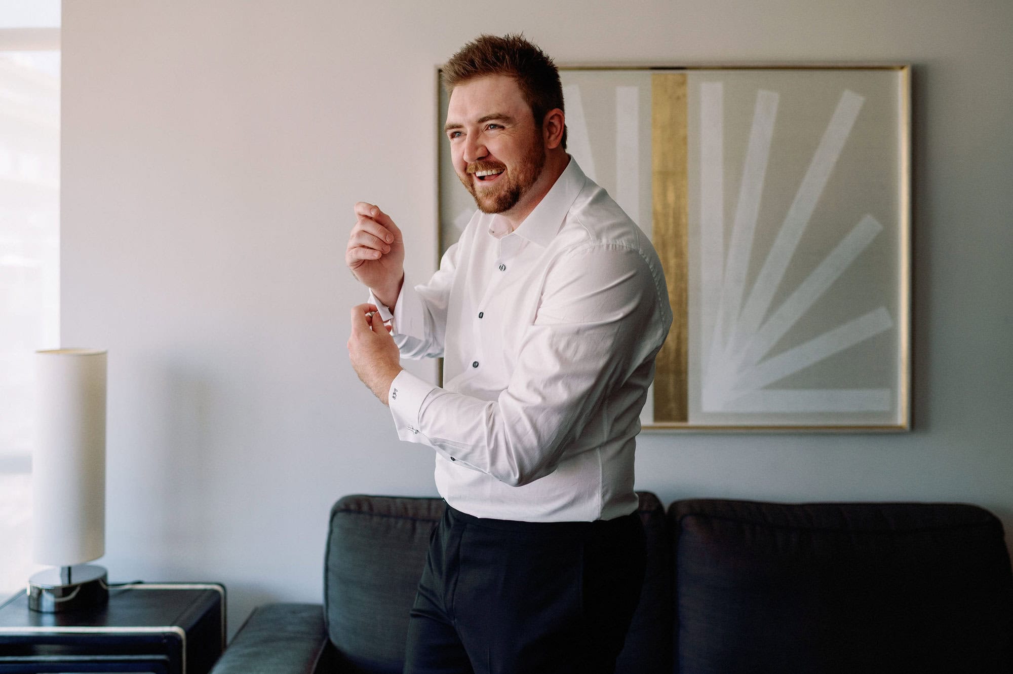 Groom laughing while fastening his cufflinks at 1 Hotel Toronto.