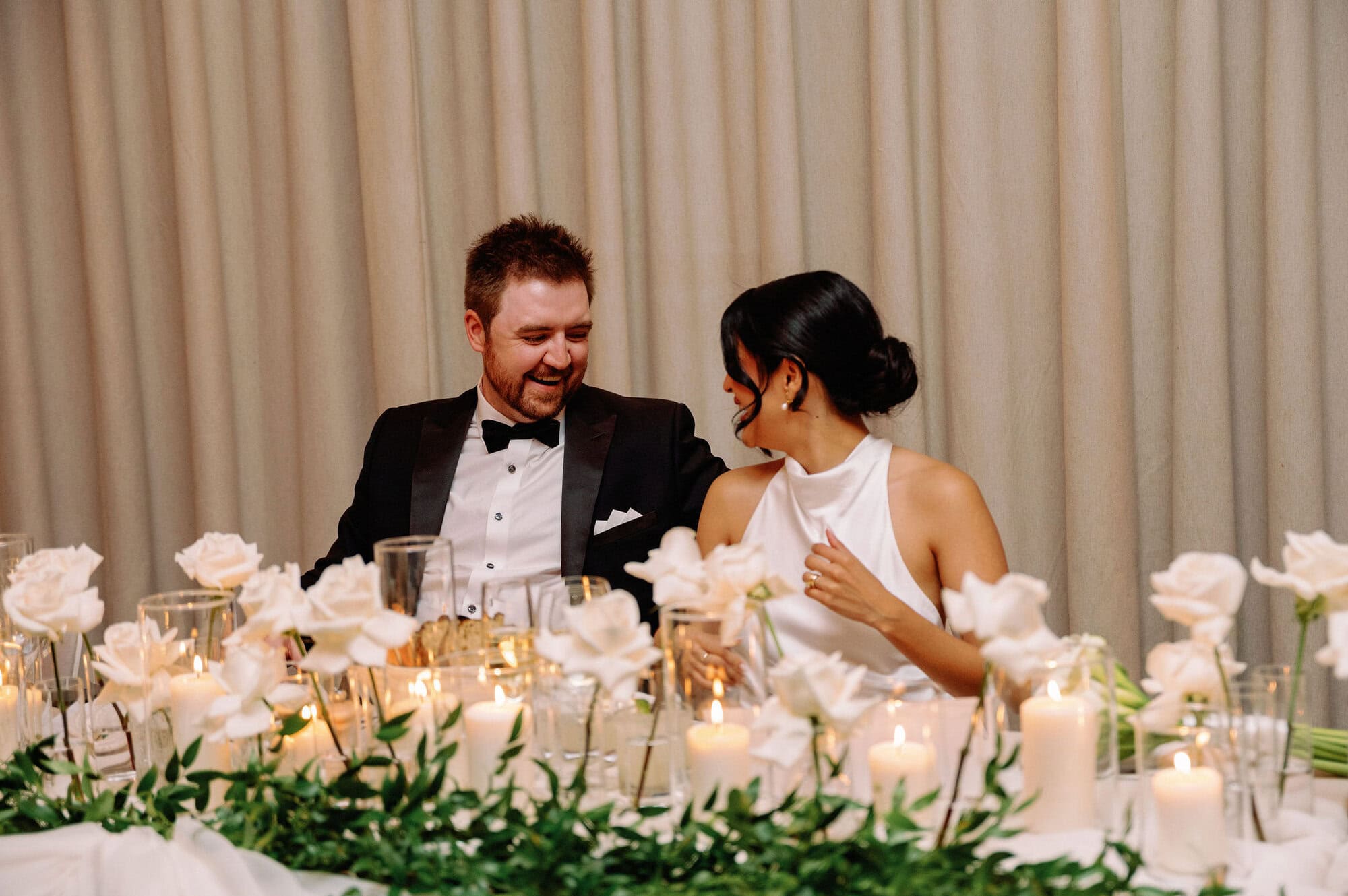 Bride and groom smiling together at their floral and candlelit head table at 1 Hotel Toronto.