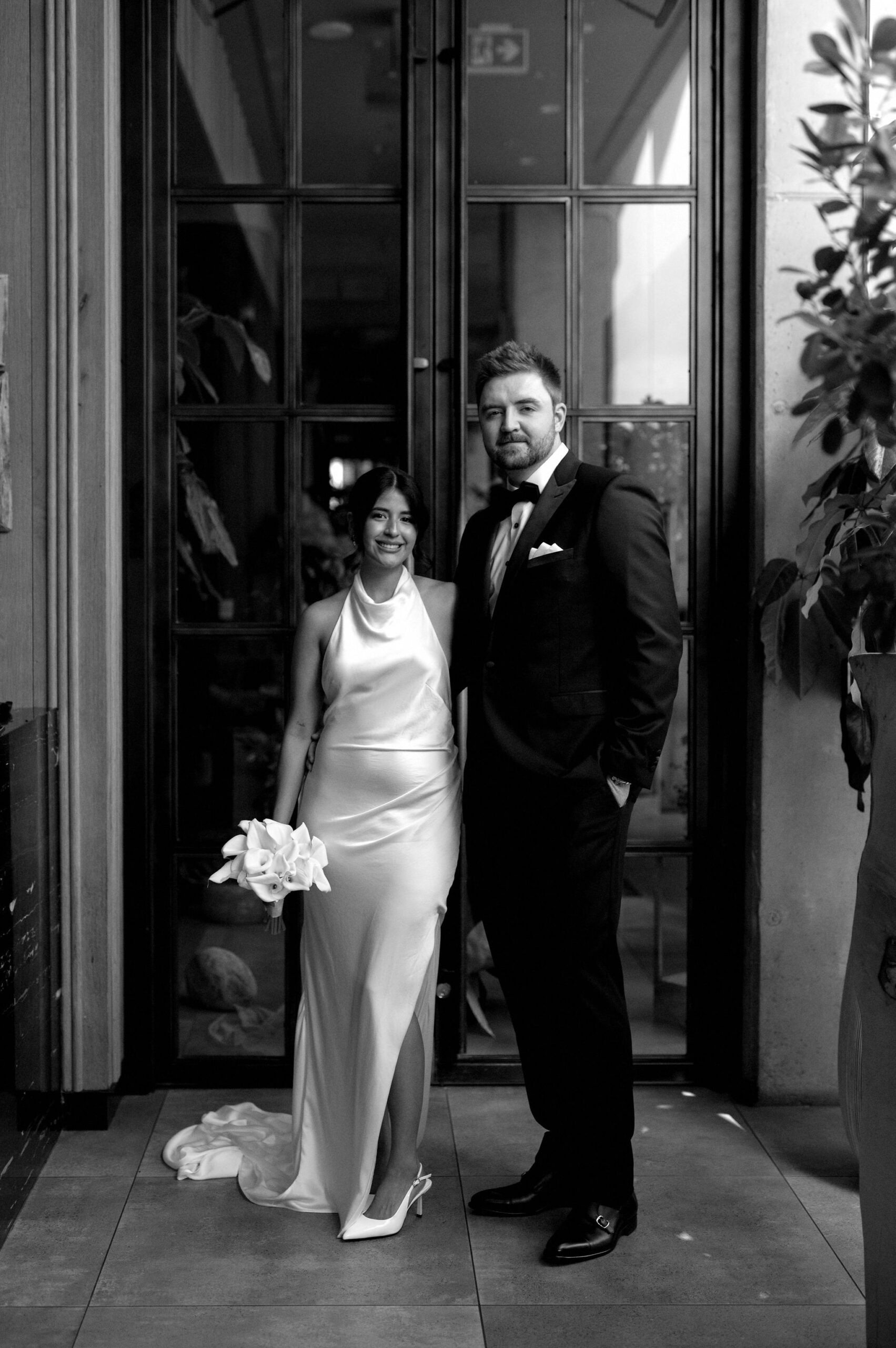 Black and white portrait of the bride and groom standing at the entrance of 1 Hotel Toronto.