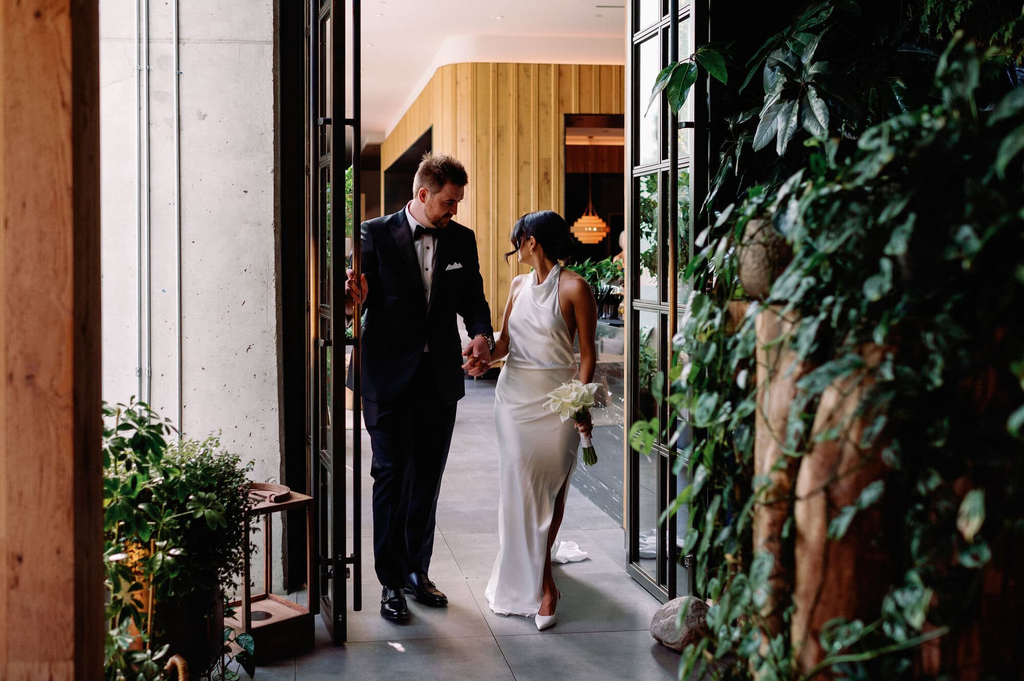 Bride and groom entering their wedding reception at 1 Hotel Toronto holding hands and smiling.
