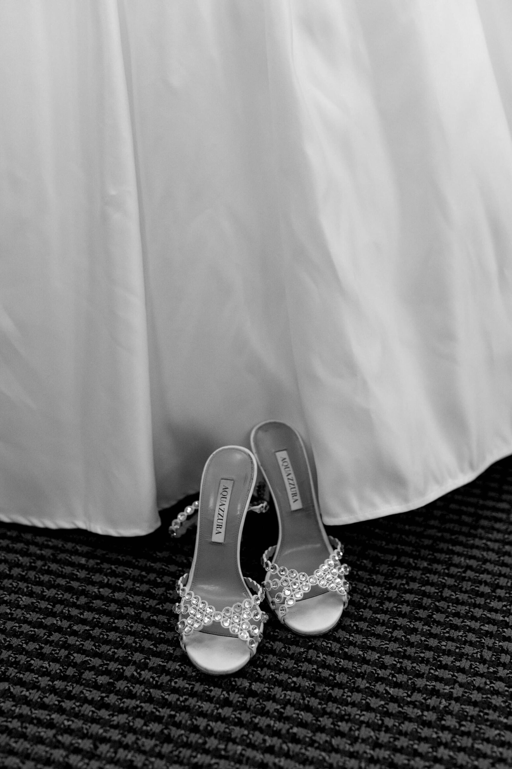 Black and white detail of the bride’s shoes placed beneath her wedding gown at Harding Waterfront Estate