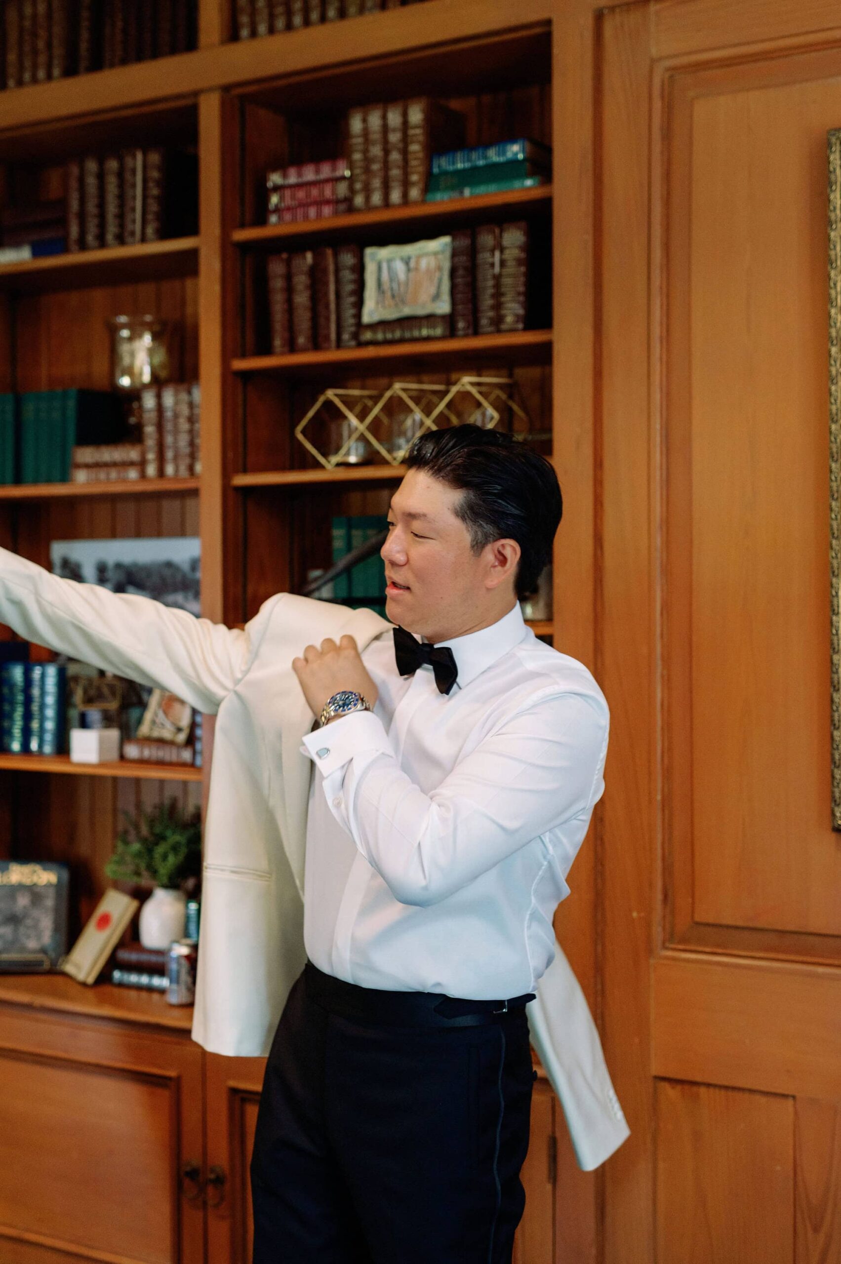 Groom standing near the bookshelves at Harding Waterfront Estate during getting ready photos.