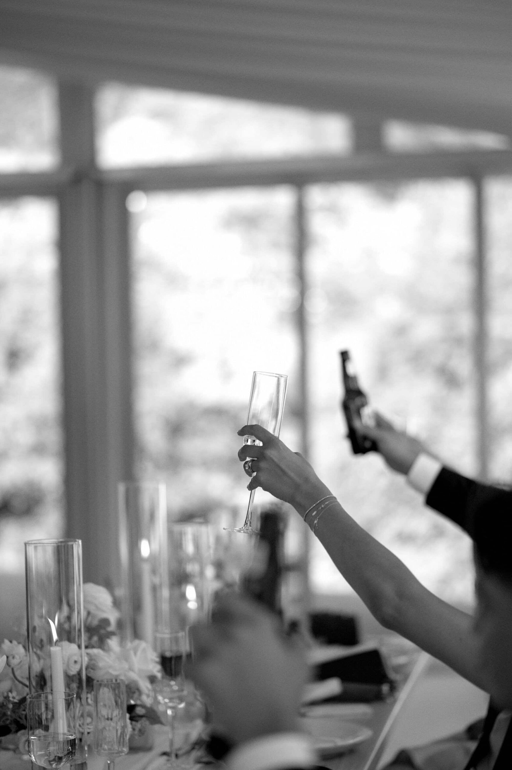 Black and white photo of guests raising glasses during the wedding reception at Harding Waterfront Estate in Mississauga.