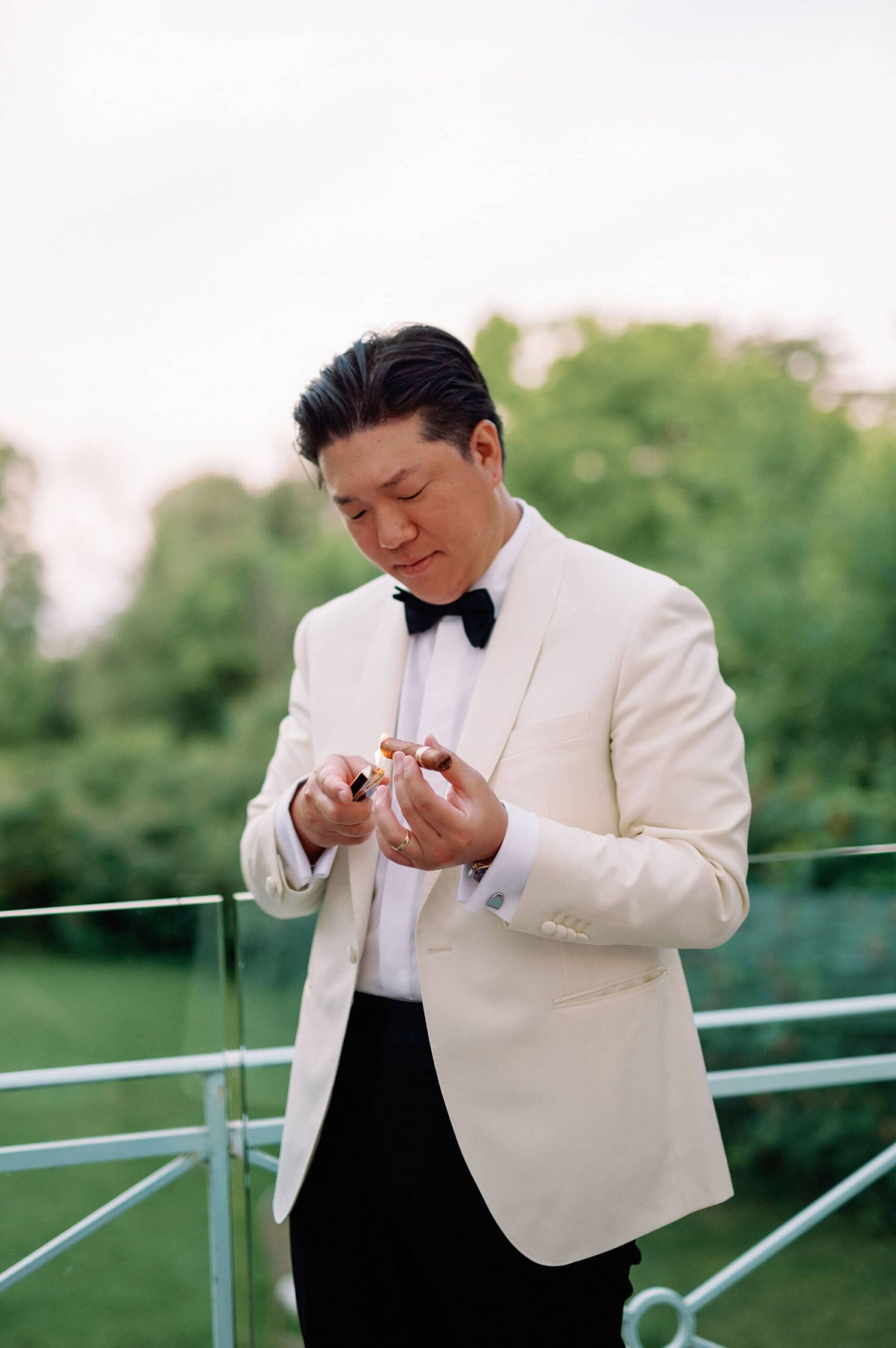Groom lighting a cigar while standing outdoors at Harding Waterfront Estate.