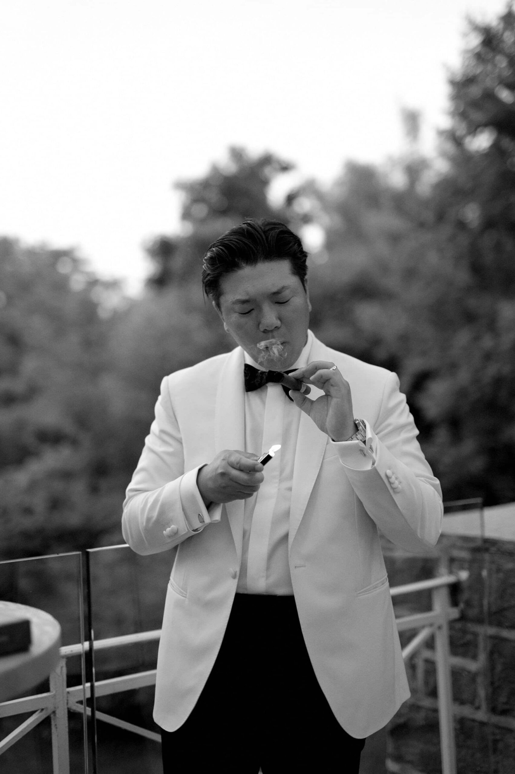 Groom lighting a cigar during cocktail hour at Harding Waterfront Estate in a black and white portrait.