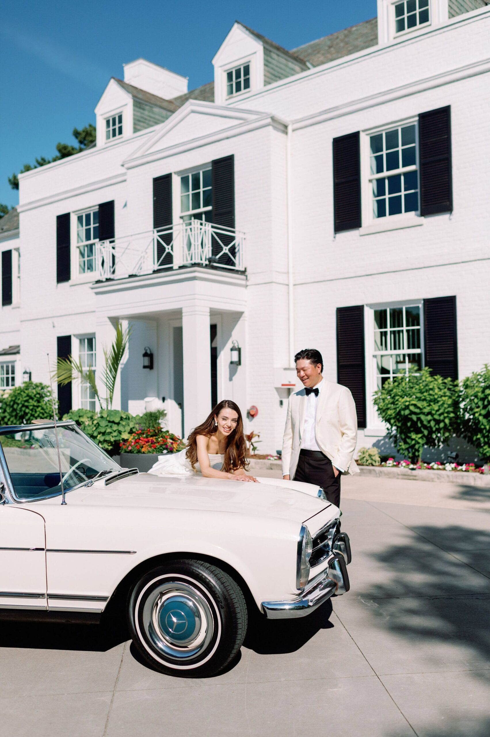 Bride and groom posing beside a vintage white convertible at Harding Waterfront Estate