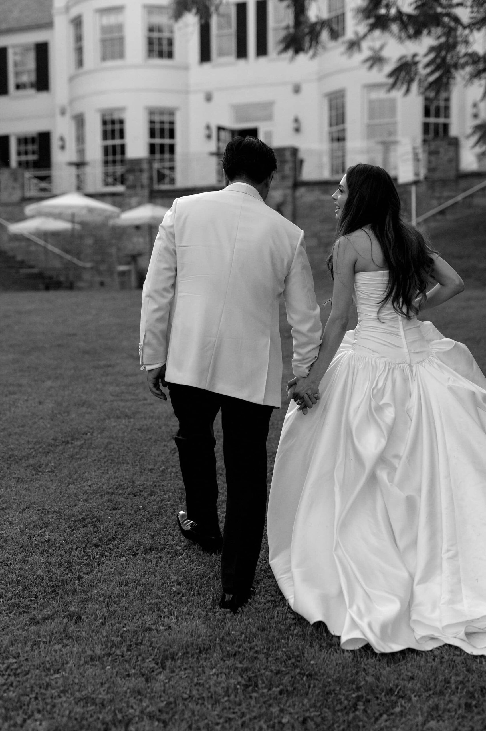 Bride and groom walking hand in hand across the lawn at Harding Waterfront Estate