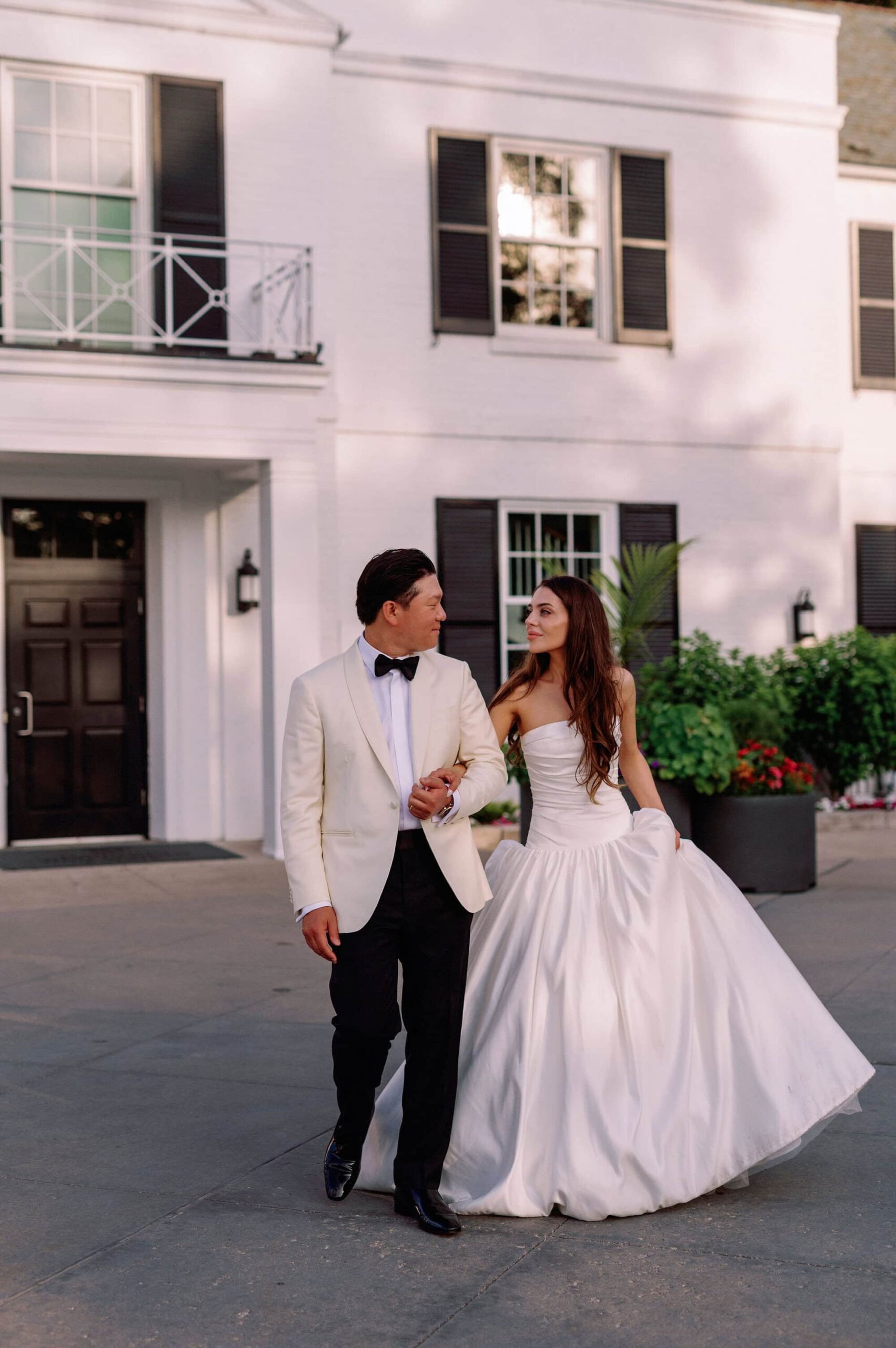 Bride and groom holding hands and smiling in front of Harding Waterfront Estate in Mississauga.
